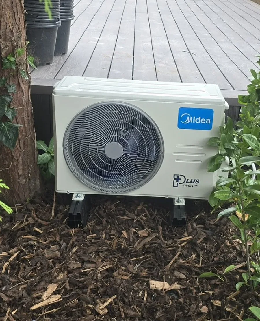 The outdoor unit of a genuine JC Heating & Cooling installation in a landscaped garden